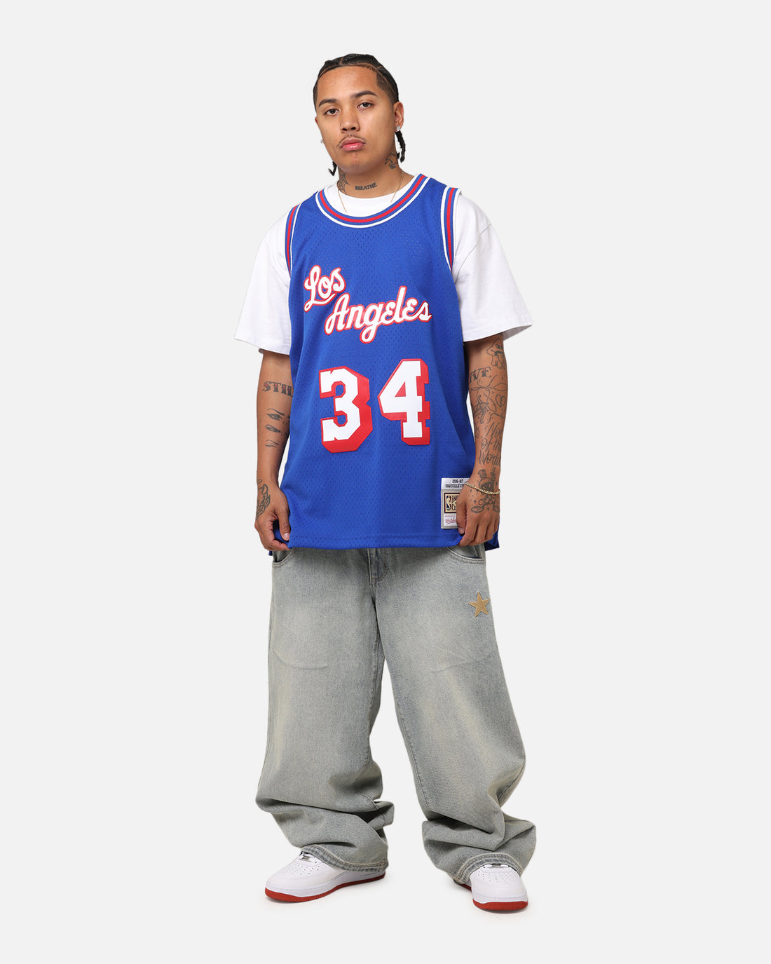 Blue basketball jersey layered over a white T-shirt with loose faded jeans and white sneakers